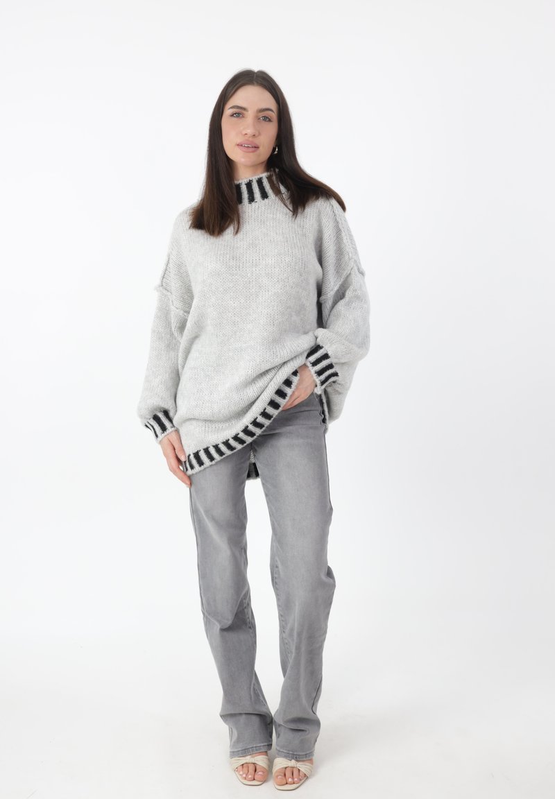 Maglione grigio oversize a maglia con accenti a righe nere sul collo e sull'orlo, abbinato a jeans dritti grigio chiaro e sandali con punta aperta.