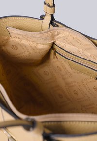 Interno di una borsa in pelle beige con una texture liscia. Presenta una tasca con zip e foderato con logo stampato, mostrando una disposizione organizzata.