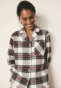 Plaid button-up shirt in soft fabric features red, blue, and gray stripes, with a pocket and contrasting collar detail.
