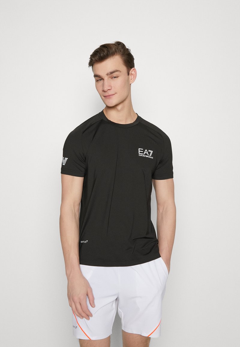 Camisa deportiva negra de manga corta con cuello redondo, que presenta el logo blanco de EA7, textura suave y mangas raglán.