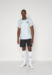 Sinivalkoinen kuvioitu urheilupaita mustien shortsien kanssa. Mukana valkoiset sukat ja urheilulliset kengät. Kevyt kangas ja moderni istuvuus.