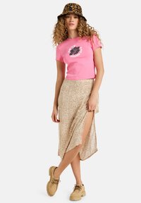 Pink cropped t-shirt with a leaf graphic, beige midi skirt featuring an abstract pattern and a side slit, paired with tan lace-up shoes.