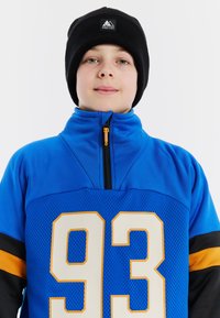 Niebieska polarowa kurtka z czarnymi i pomarańczowymi akcentami, z wysokim kołnierzem i dużym białym napisem "93" z przodu. Czarna czapka na głowie.