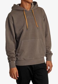 Bruine hoodie met een trekkoordcapuchon, kangaroo pocket en geribbelde manchetten. Heeft een subtiel logo in het midden en contrasterende oranje trekkoorden.