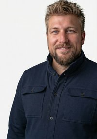 Donkerblauw stoffen overhemd met een licht gestructureerd ontwerp, voorzien van twee borstzakken met knopen en een hoge kraag met een knoopsluiting.