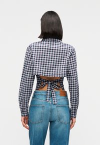 Καρό κοντομάνικο πουκάμισο σε ναυτικό μπλε, λευκό και κόκκινο, με μακριά μανίκια και δέσιμο στο πίσω μέρος. Συνδυασμένο με ψηλόμεσα μπλε τζιν παντελόνια.