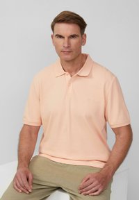 Hellbeige Polo-Shirt mit Kragen, kurzen Ärmeln und einem dezenten Logo. Hergestellt aus weichem Stoff und mit einer klassischen Knopfleiste ausgestattet.