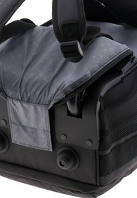 Borsa a tracolla nera con una sezione interna grigia imbottita, dettagli in rete, chiusura con cerniera e spallacci regolabili. Presenta motivi circolari sul tessuto.