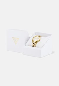 Orologio da polso in tono oro con quadrante bianco, bracciale in maglia dorata testurizzata e accenti di gemme, presentato in una confezione bianca con logo dorato.
