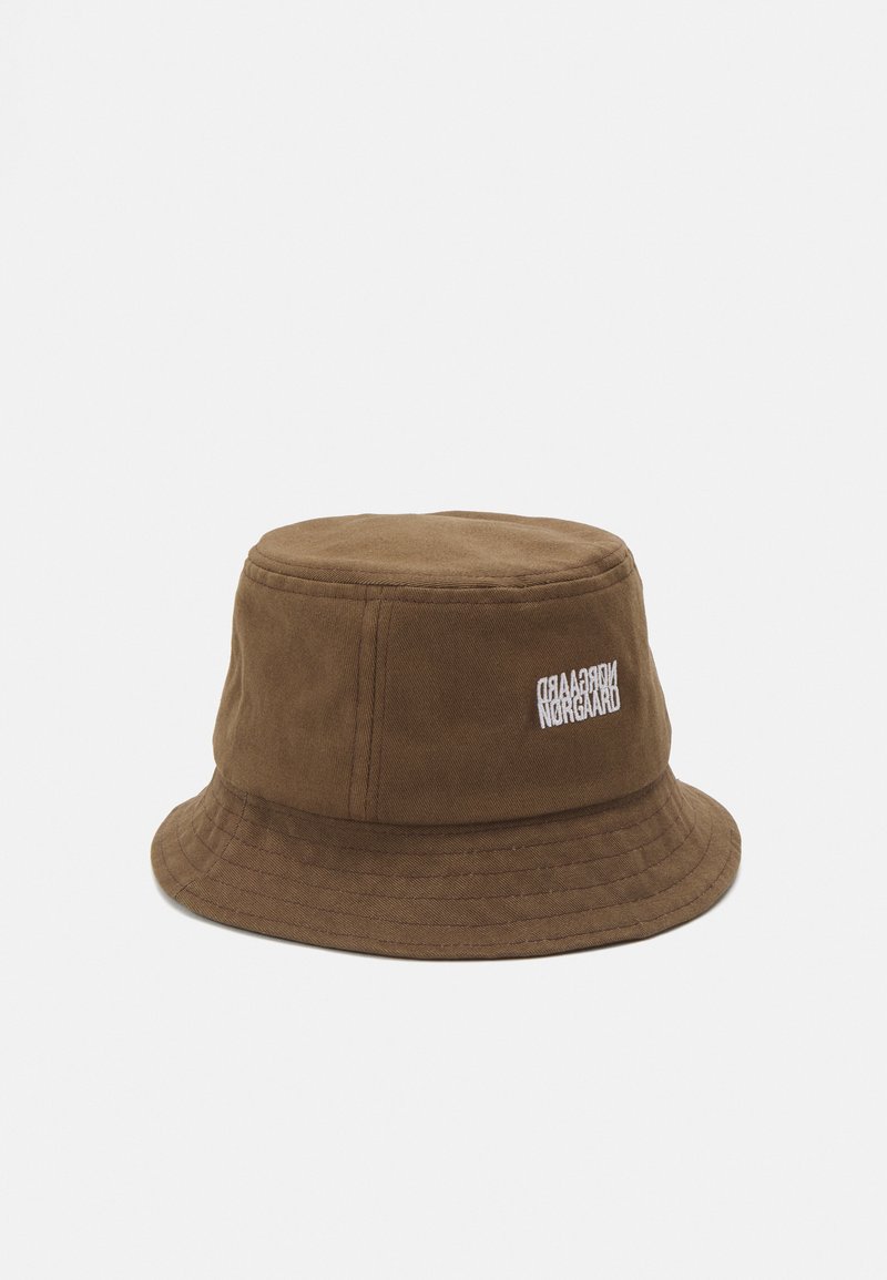 Brun bomullsbøttehatt med en rund, fleksibel brem, med en hvit brodert logo på siden. Glatt tekstur og lett design.