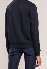 Felpa blu navy con collo rotondo, maniche lunghe e polsini a coste. Abbinata a jeans denim blu scuro. Tessuto dalla consistenza liscia.