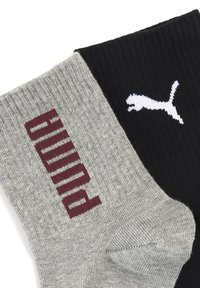Szare i czarne skarpetki; szara skarpetka ma czerwony napis "PUMA" i prążkowaną teksturę; czarna skarpetka ma białe logo, również prążkowane.