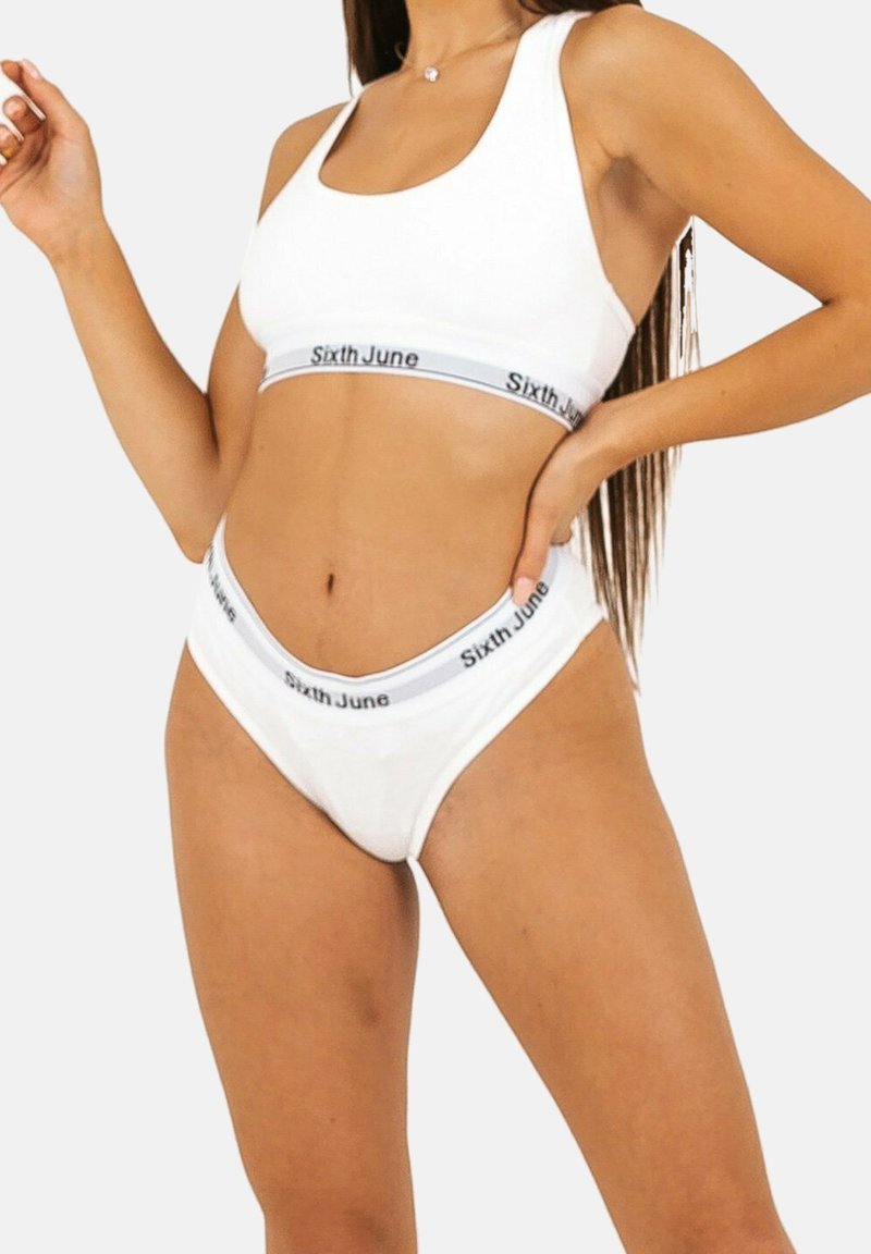 Reggiseno sportivo bianco e set di biancheria intima abbinato realizzati in un tessuto morbido, con bande grigie a contrasto riportanti il testo "Sixth June" su ogni pezzo.