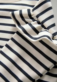 Witte katoenen stof met verticale navy strepen, met een gerimpelde mouwdetail. De textuur lijkt zacht en licht van gewicht.