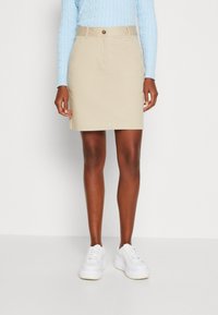 Beige bomullskjol med rak skärning, knäppning och fickor, i kombination med vita sneakers och en ljusblå kabelstickad tröja.