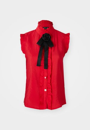 Rød kortermet bluse med volangkrage, dekorativ svart rose og knappefront med hvite blomsterformede knapper; glatt, lett stoff.