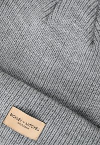 Graue gestrickte Mütze mit gerippter Struktur. Enthält ein beiges Etikett mit "BICKLEY + MITCHELL AMSTERDAM" in Schwarz bedruckt.