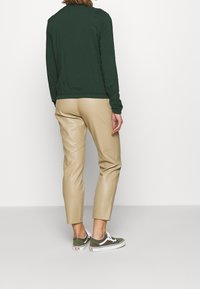 Chemise verte à manches longues, pantalon beige sur mesure et baskets vertes. La tenue associe des textures douces à une coupe ajustée.