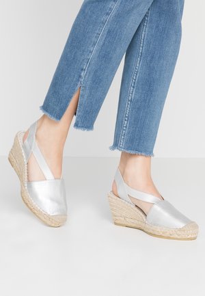 Sandales espadrilles à talon compensé en métal argenté avec une semelle en jute tissée, dotées d'un bout fermé et de brides croisées à la cheville. Denim avec ourlet effiloché visible.