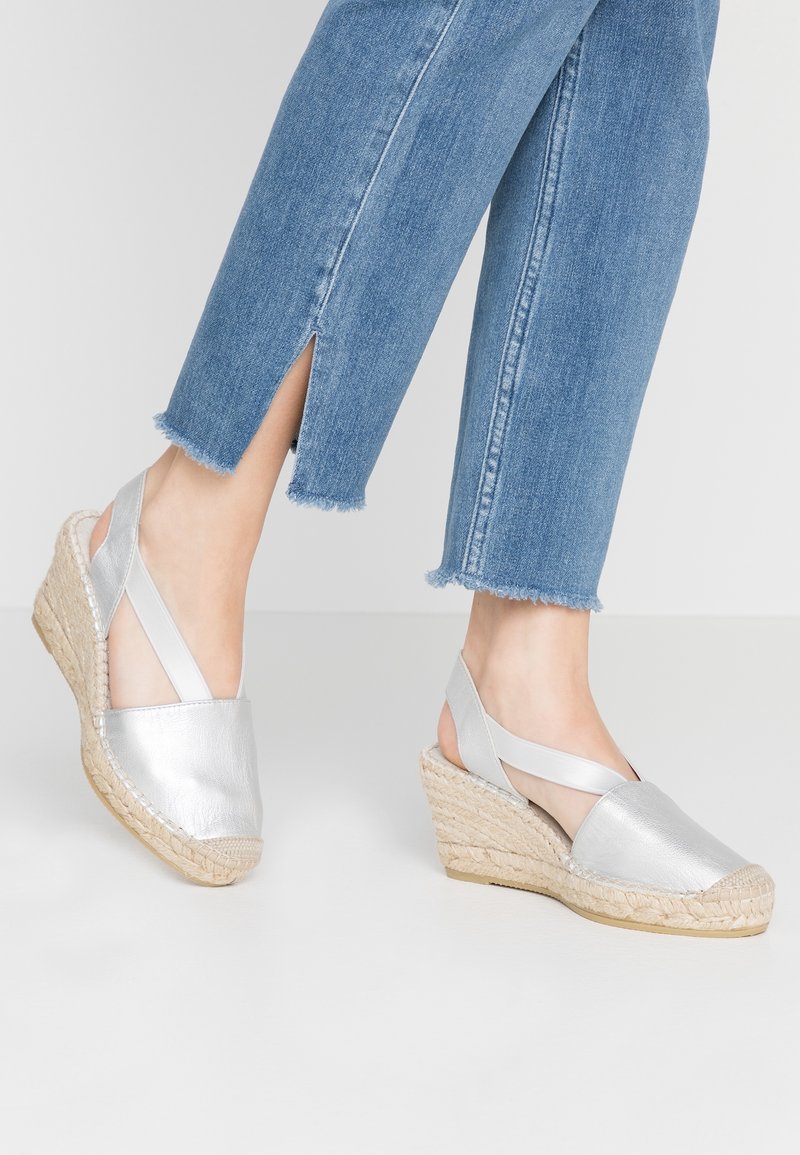 Sandales espadrilles à talon compensé en métal argenté avec une semelle en jute tissée, dotées d'un bout fermé et de brides croisées à la cheville. Denim avec ourlet effiloché visible.