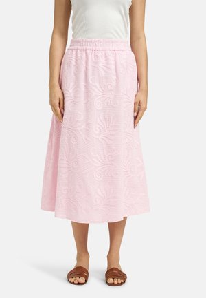 Frau trägt ein weißes ärmelloses Oberteil und einen rosa bestickten Midirock mit elastischem Bund sowie braune Sandalen mit offenen Zehen.