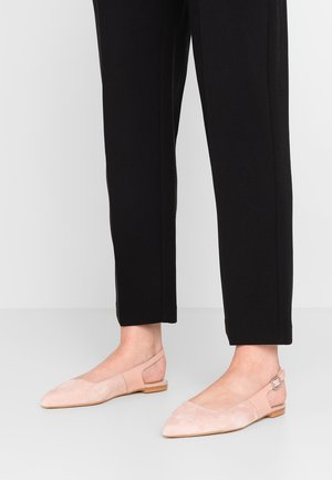 Femme portant un pantalon court noir et des ballerines slingback rose clair à bout pointu avec une bride à boucle et un petit talon en bois.