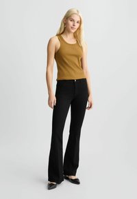 Geribbeld, mosterdkleurig tanktop met een ronde halslijn, gecombineerd met zwarte flared jeans. De outfit wordt compleet gemaakt met zwarte spitse flats.