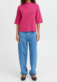 Haut fuchsia en maille côtelée avec manches larges, associé à un jean droit taille haute bleu clair et des chaussures plates noires.
