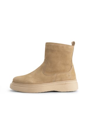 Beige suède enkellaars met dikke beige rubberen zool, een treklabel aan de achterkant en subtiele logo-embossing aan de zijkant.