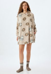 Sudadera con capucha de felpa oversized en beige con patrones de dibujos de galletas y leche. Presenta una textura suave y un bolsillo frontal.
