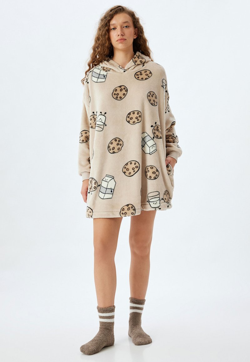 Sudadera con capucha de felpa oversized en beige con patrones de dibujos de galletas y leche. Presenta una textura suave y un bolsillo frontal.
