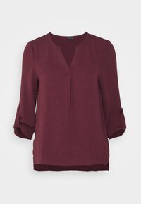 Blouse en bourgogne tissée avec un col en V, manches ¾ retroussées avec des onglets, texture subtile et ourlet droit. Idéale pour le superposition.
