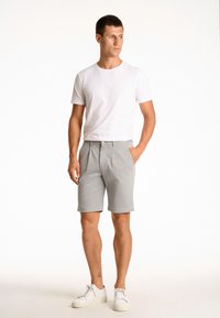 Pantaloni corti grigi chiari con fronte piatto, orlo risvoltato e due tasche laterali. Abbinati a una maglietta bianca aderente e sneakers bianche.