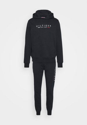 Czarna bluza z kapturem i dopasowane spodnie dresowe z logo "Hilfiger New York" w białym, czerwonym i szarym kolorze na klatce piersiowej oraz nodze.