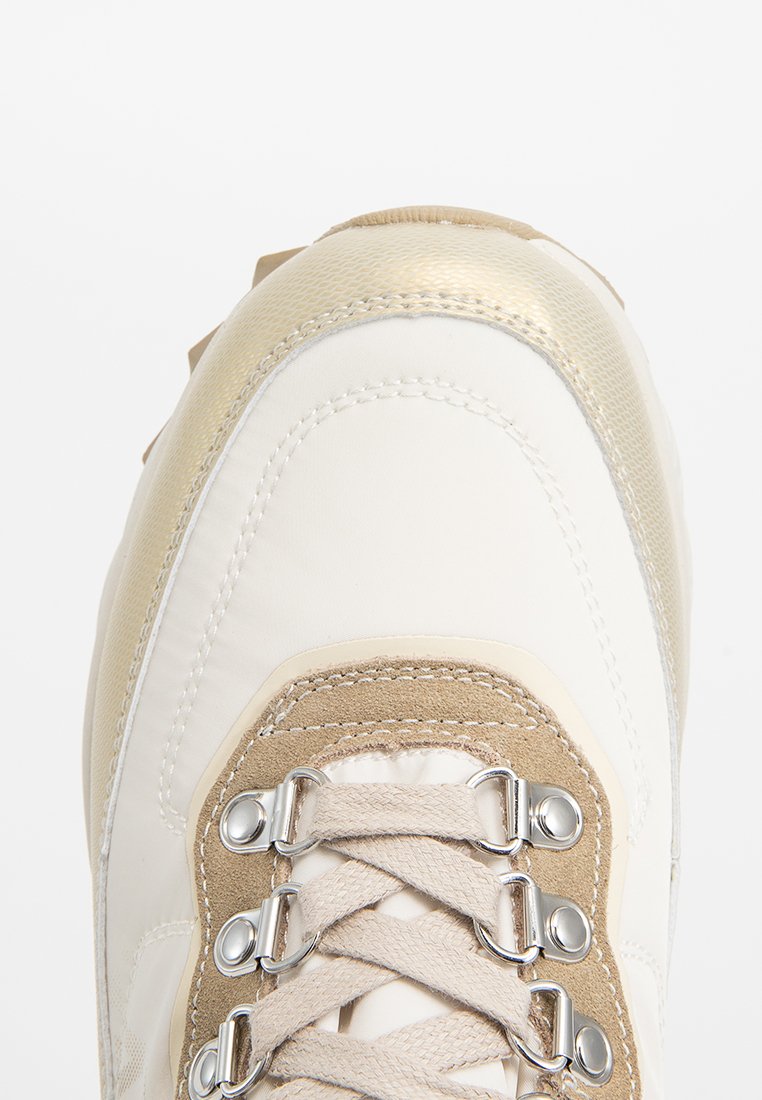 Witte en gouden sneaker met een glad leren bovenmateriaal, suède accenten, metalen veterogen en een gestructureerd paneel langs de teen.