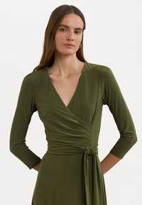 Abito avvolgente verde oliva con maniche lunghe, scollatura a V e dettaglio con nodo laterale. Realizzato in tessuto morbido con una silhuette aderente.