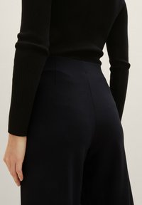 Top nero a coste a maniche lunghe abbinato a pantaloni fitted scuri blu navy a vita alta. Texture liscia con cuciture sartoriali e dettagli discreti.