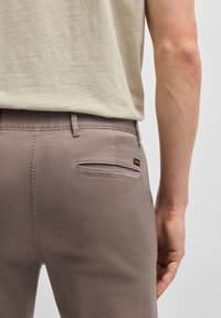 T-shirt beige clair assorti avec un pantalon gris-brun. Le pantalon dispose d'une poche arrière avec une étiquette de marque et est en tissu léger et lisse.