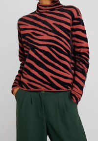 Maglione a collo alto a righe zebrate in tessuto morbido ruggine e nero, con una vestibilità rilassata, maniche lunghe e dettagli a coste sul collo.