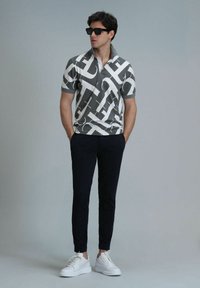 Kurzarm-Polo in Grau mit weißem abstraktem Muster, kombiniert mit navyfarbenen Hosen und weißen Sneakers. Model trägt schwarze Sonnenbrillen.