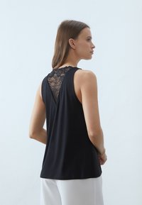Top negro sin mangas con detalle de encaje en la espalda, corte en forma de V y textura suave. Diseño simple y ajuste relajado.