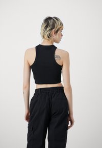 Black ribbed sleeveless crop top with a fitted design. Worn with dark, loose-fitting cargo pants featuring an elastic waistband.