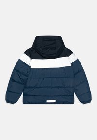 Veste rembourrée en marine, blanc et bleu foncé. Dispose d'une capuche, de blocs de couleur horizontaux et de poignets élastiques. Texture lisse avec une finition légèrement brillante.