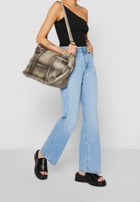Metallic silver axelväska med vadderade sektioner, justerbar rem, i kombination med ljusblå utsvängda jeans och svarta platåsandaler.