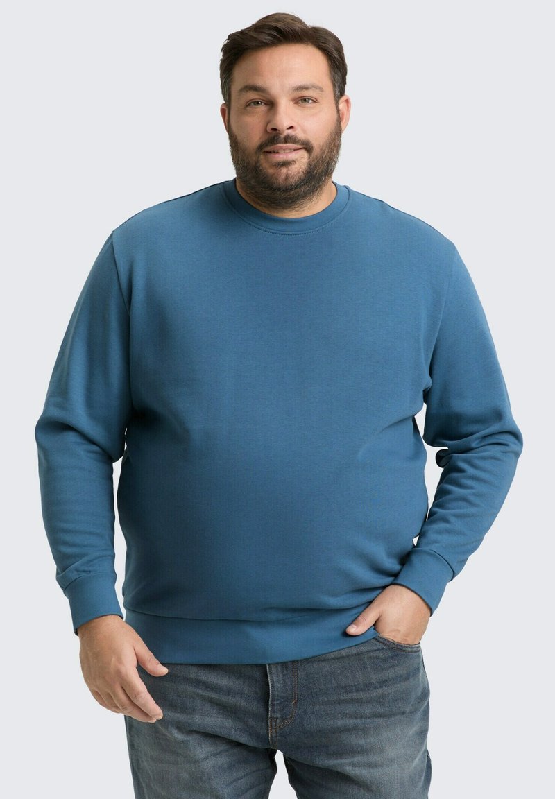 Zils kokvilnas krekls ar garām piedurknēm, apļa kakla izgriezumu un ribotām piedurknēm, pāris ar džinsu biksēm. Gluda tekstūra, brīva piegriezuma.