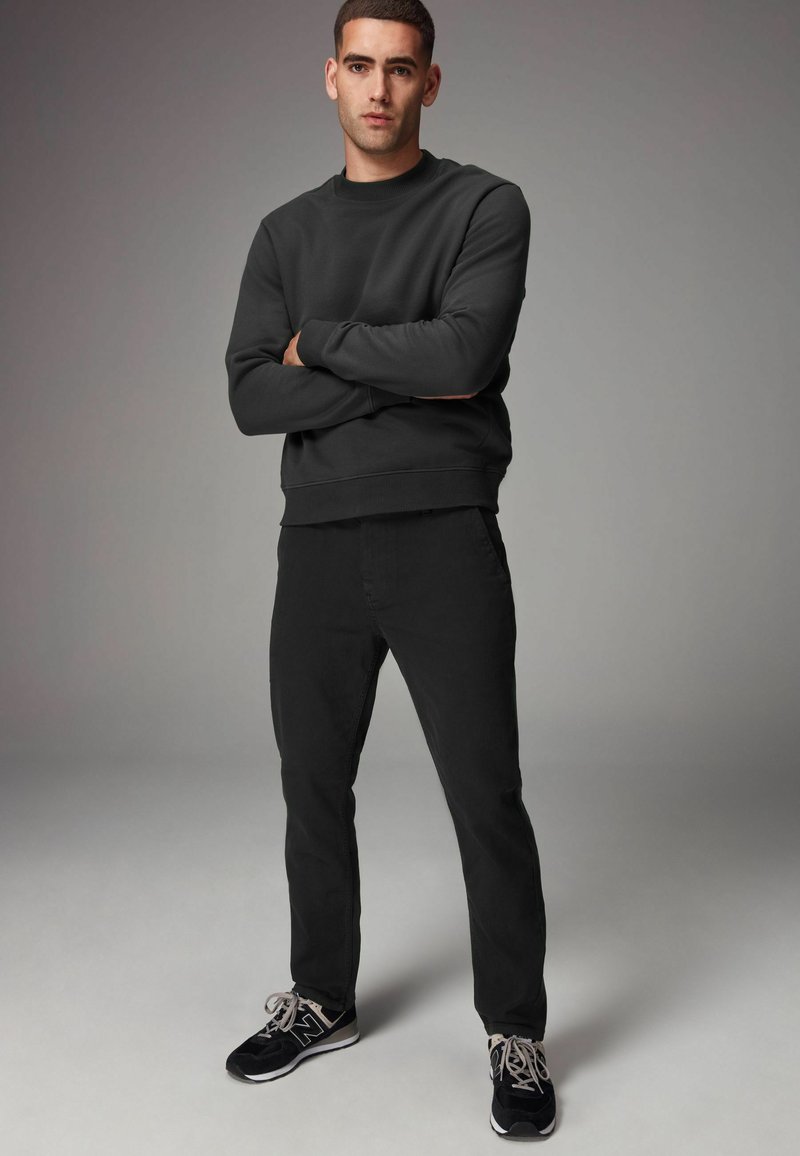 Sort sweatshirt med rund hals, parret med sorte slim-fit jeans og sorte sneakers. Enkel, ensartet farveskala uden mønstre.