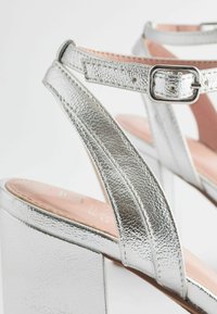 Sandales à talons argentées avec un dessus metallic texturé, design à deux brides, boucle ajustable et un large talon bloc.