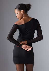Robe noire ajustée avec de longues manches transparentes et un décolleté asymétrique. Présente un design froncé à l'arrière et une texture lisse.