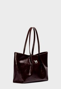 Bruine leren tote bag met twee lange handvatten, met een glanzende afwerking en een zilveren logodetail aan de voorkant. Ruimtelijk en minimalistisch ontwerp.