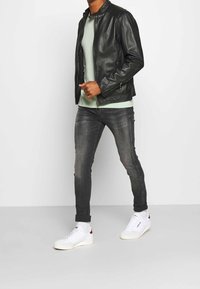Chaqueta de cuero negra con cuello alto, combinada con una camiseta verde claro, jeans gris ajustados y zapatillas blancas con detalles rojos.